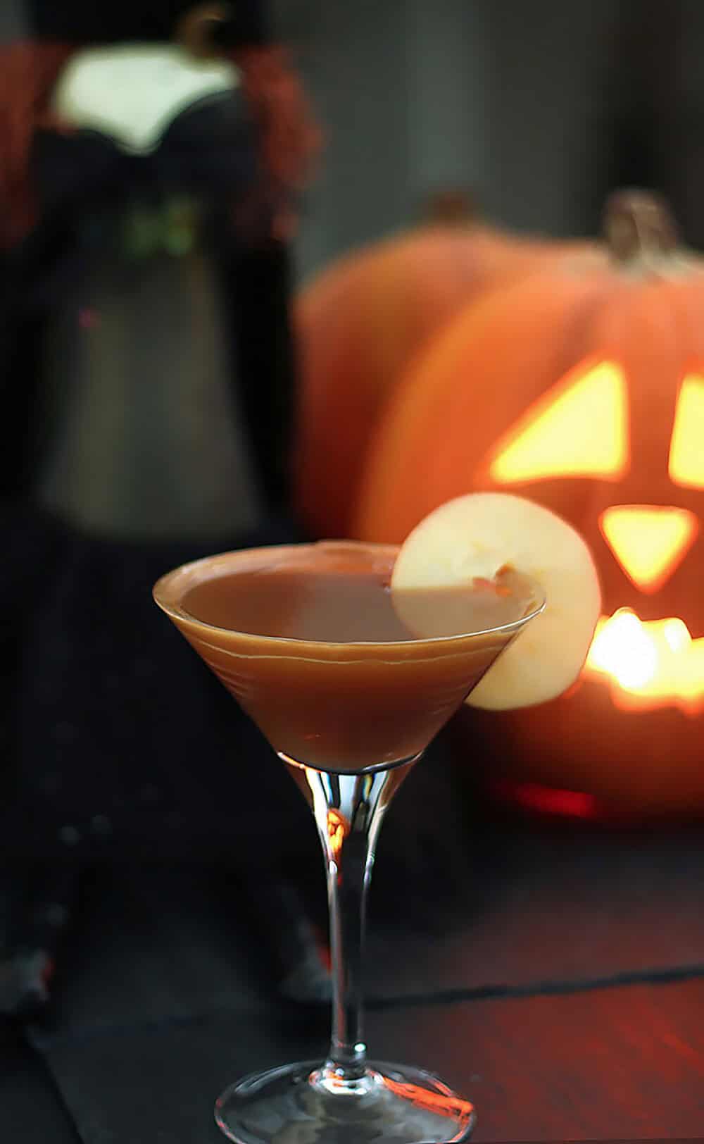 Caramel Apple Martini in a glass with Halloween pumpkin decoration.