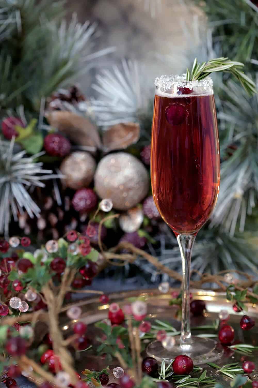 Beautiful Cranberry Poinsettia Cocktail with a burgundy beverage sitting in front of a white birdhouse decorated with a red Cardinal.