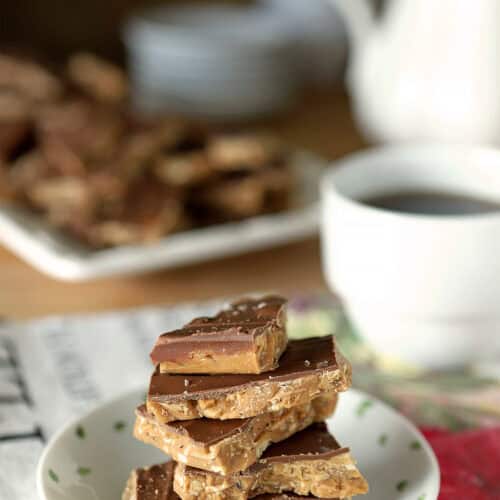 White plate with English Toffee pieces stacked and accompanied by a cup of coffee.