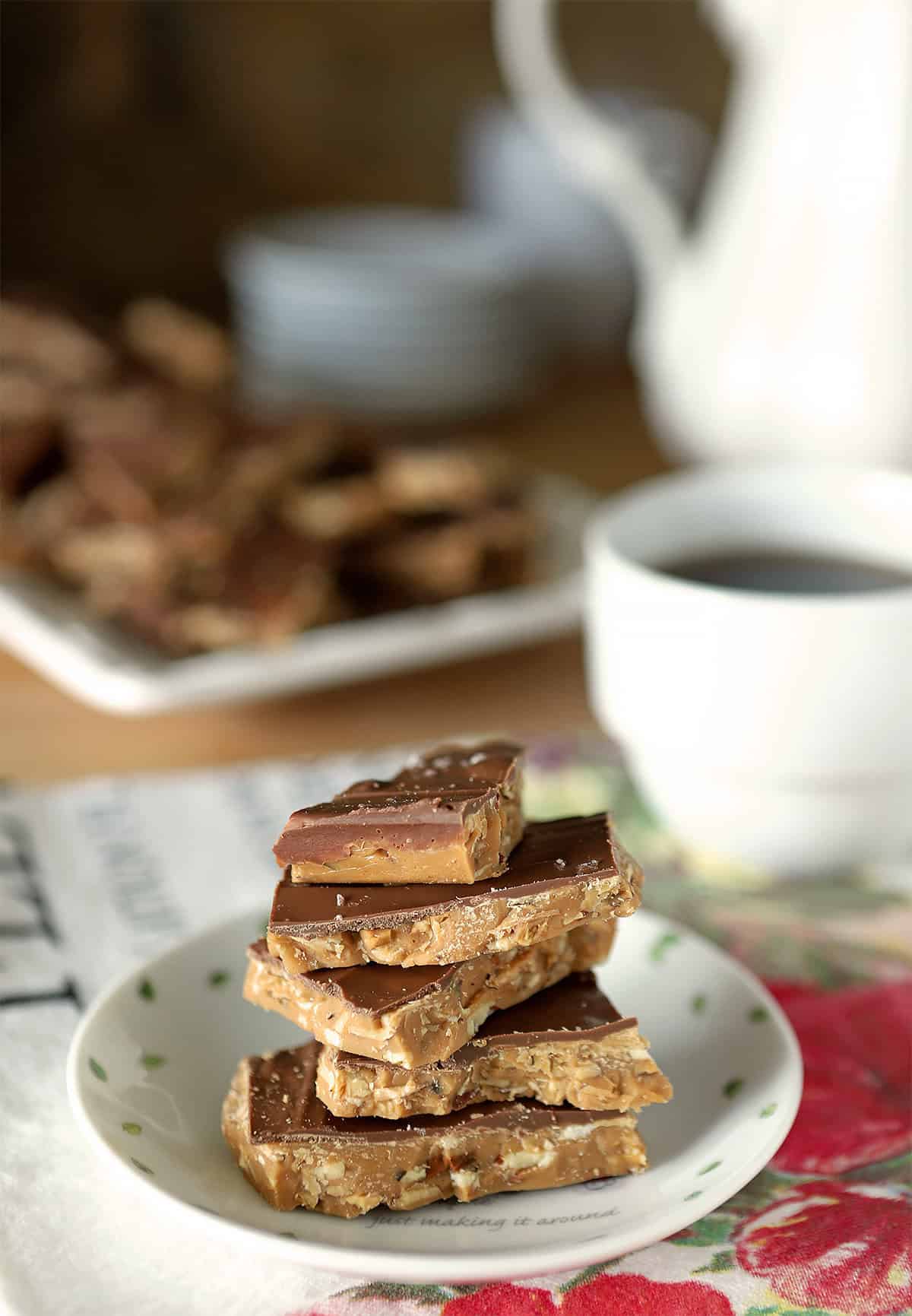 White plate with English Toffee pieces stacked and accompanied by a cup of coffee.