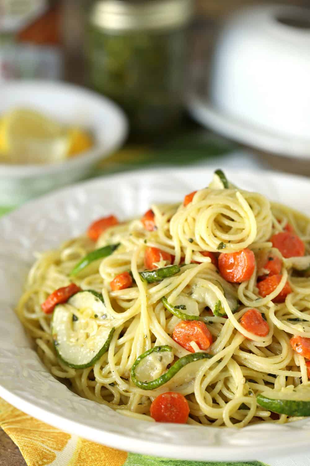 Close-up of garlic pesto pasta with carrots and zucchini on a white plate.