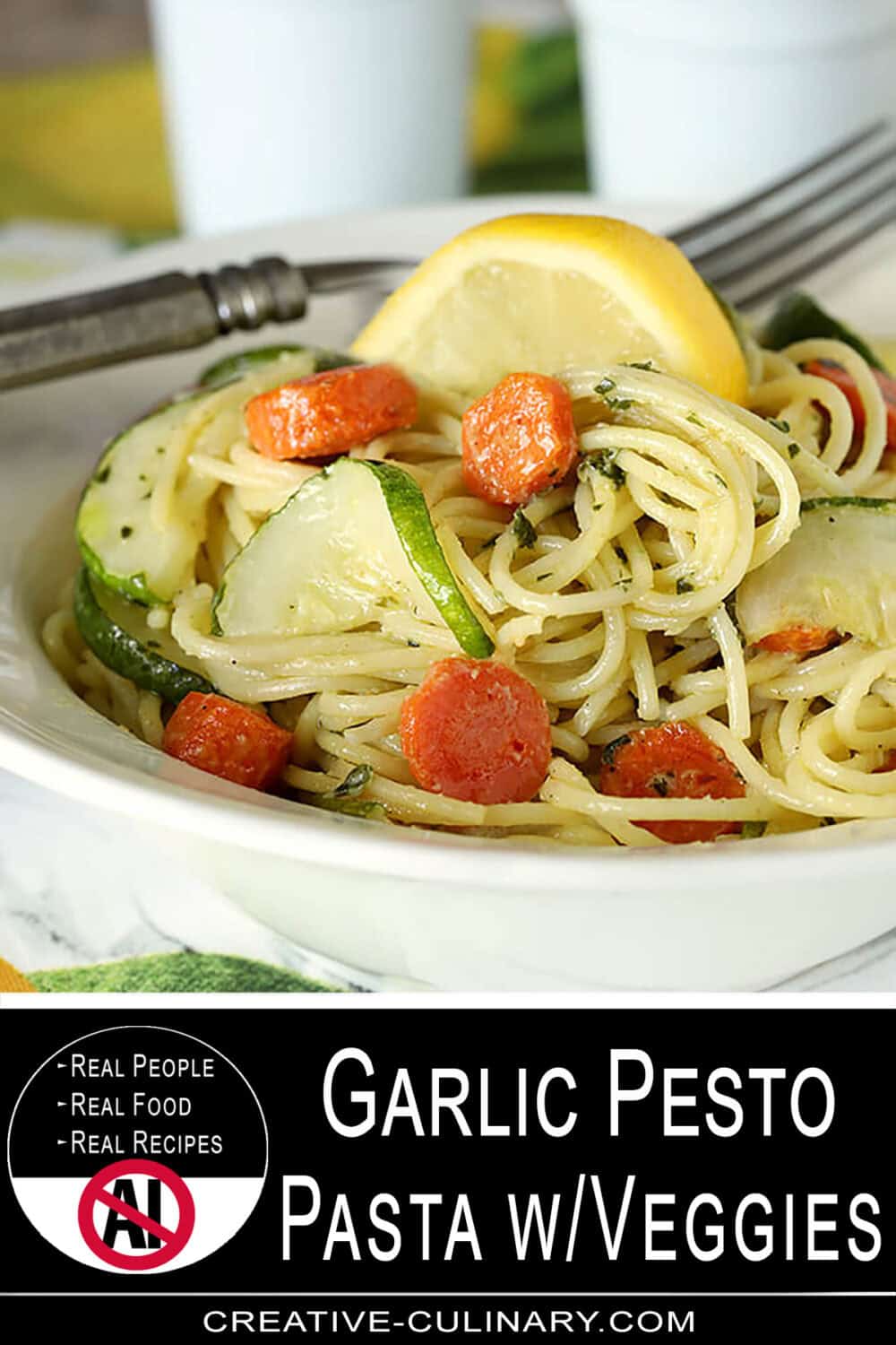 Close-up of garlic pesto pasta with carrots, zucchini, and lemon wedge.