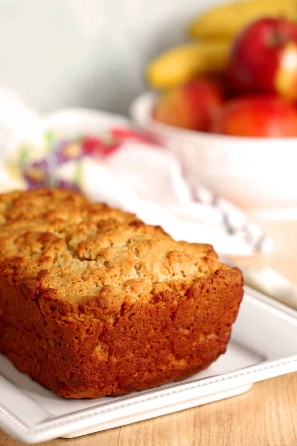 Close-up of honey butter beer bread on a white plate with fresh fruit in background.