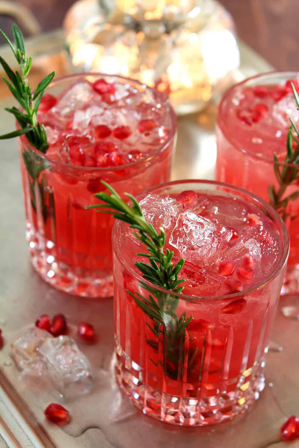 Pomegranate and Rosemary Gin Fizz in a lowball cut crystal glass; garnished with a spring of rosemary and pomegranate arils.
