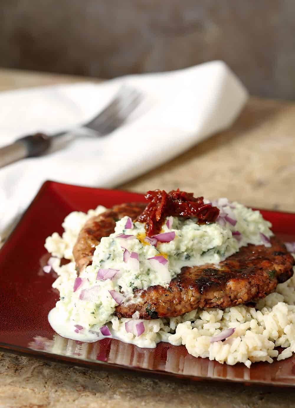 Greek veggie burger served with creamy tzatziki sauce and rice on a red plate.