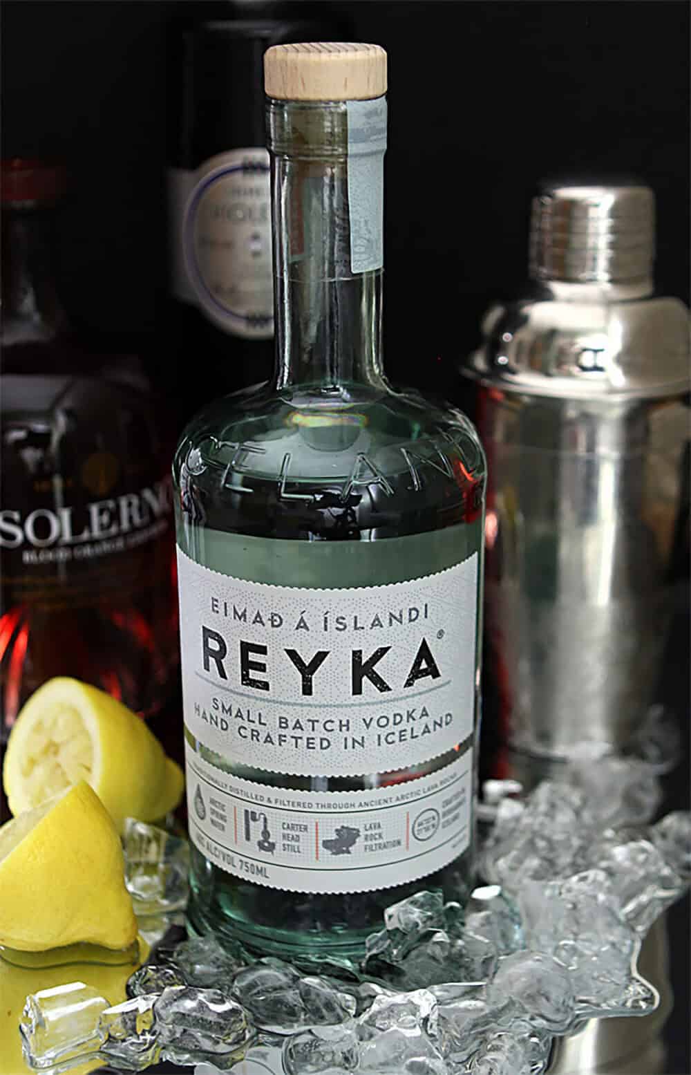 Reyka small batch Icelandic vodka bottle on ice with lemons and bar tools.
